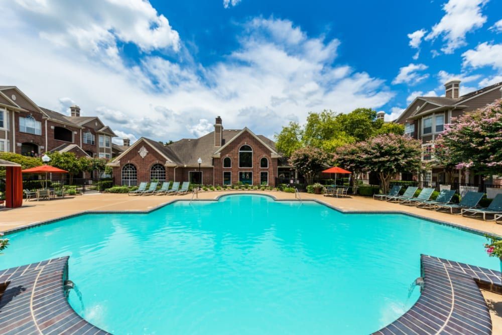 a large swimming pool surrounded by chairs and umbrellas in front of a brick building at Marquis on Park Row in Houston, TX.
