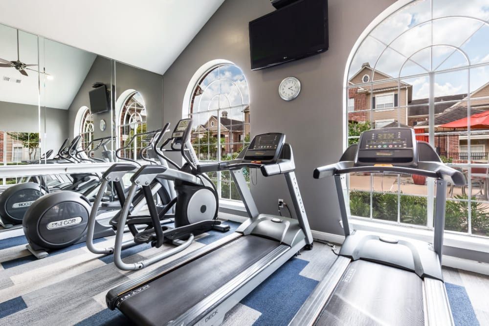a gym with treadmills, ellipticals, and a television at Marquis on Park Row in Houston, TX.