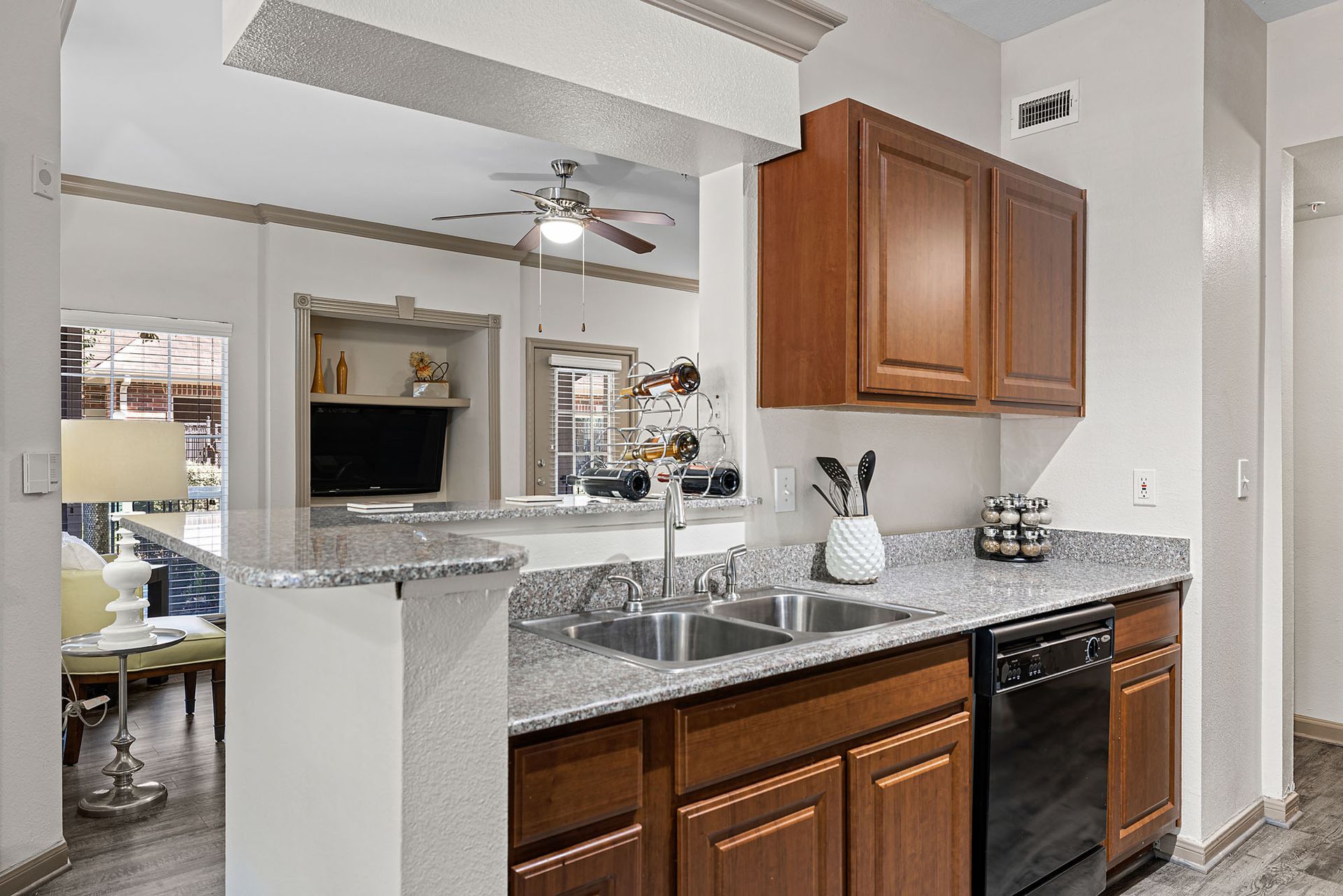 Kitchen in an apartment with granite countertops, double sink, wooden cabinets, and a dishwasher.