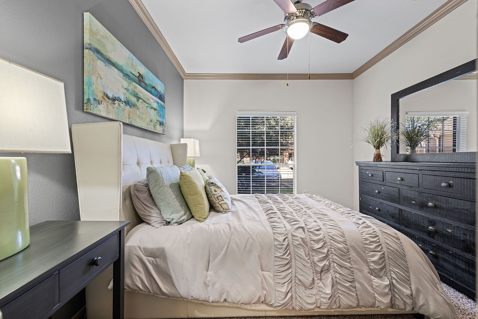 Bedroom with a large bed, nightstands, a dark dresser, and a ceiling fan by a window.