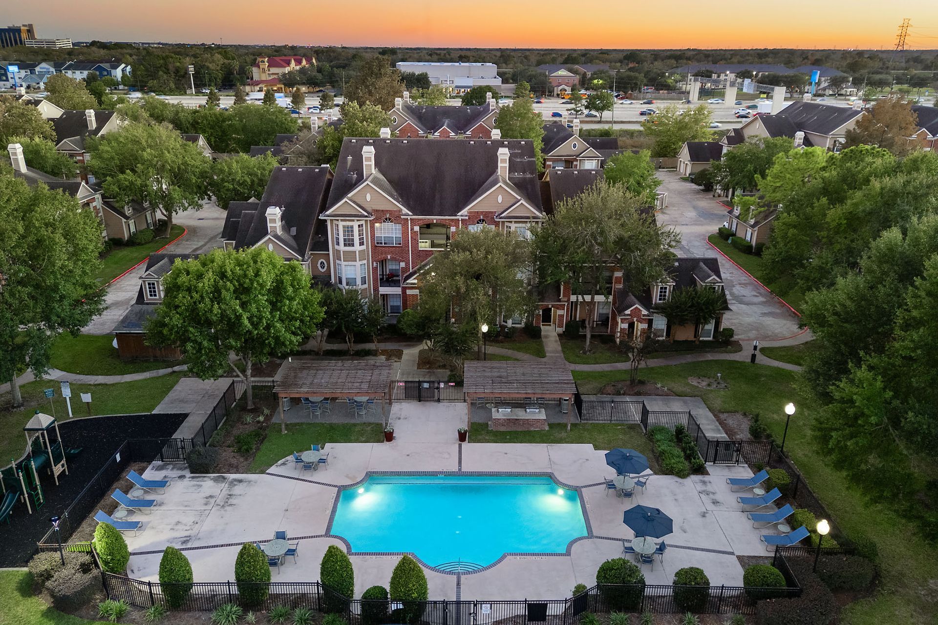 Aerial view of a community pool at a multifamily complex with brick buildings and surrounding trees.