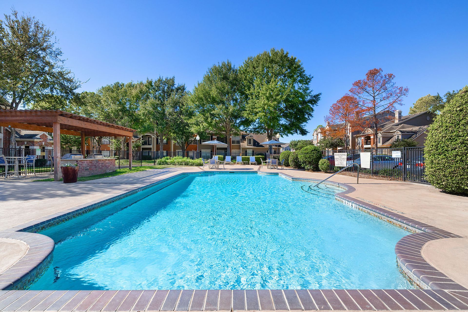 Outdoor apartment community pool with lounge chairs and trees.