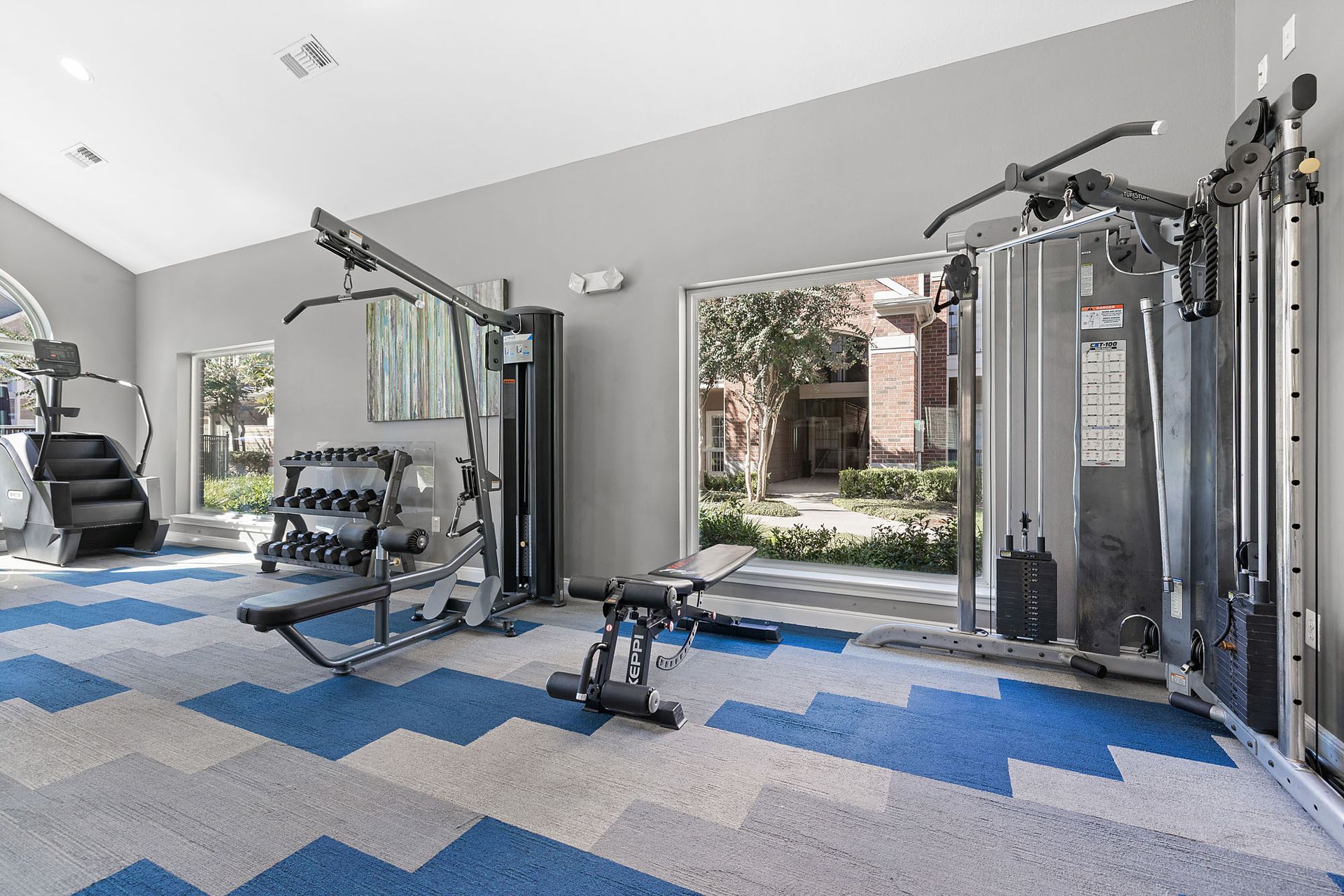 Bright residential gym with cardio machines, free weights, and a multi-station setup.