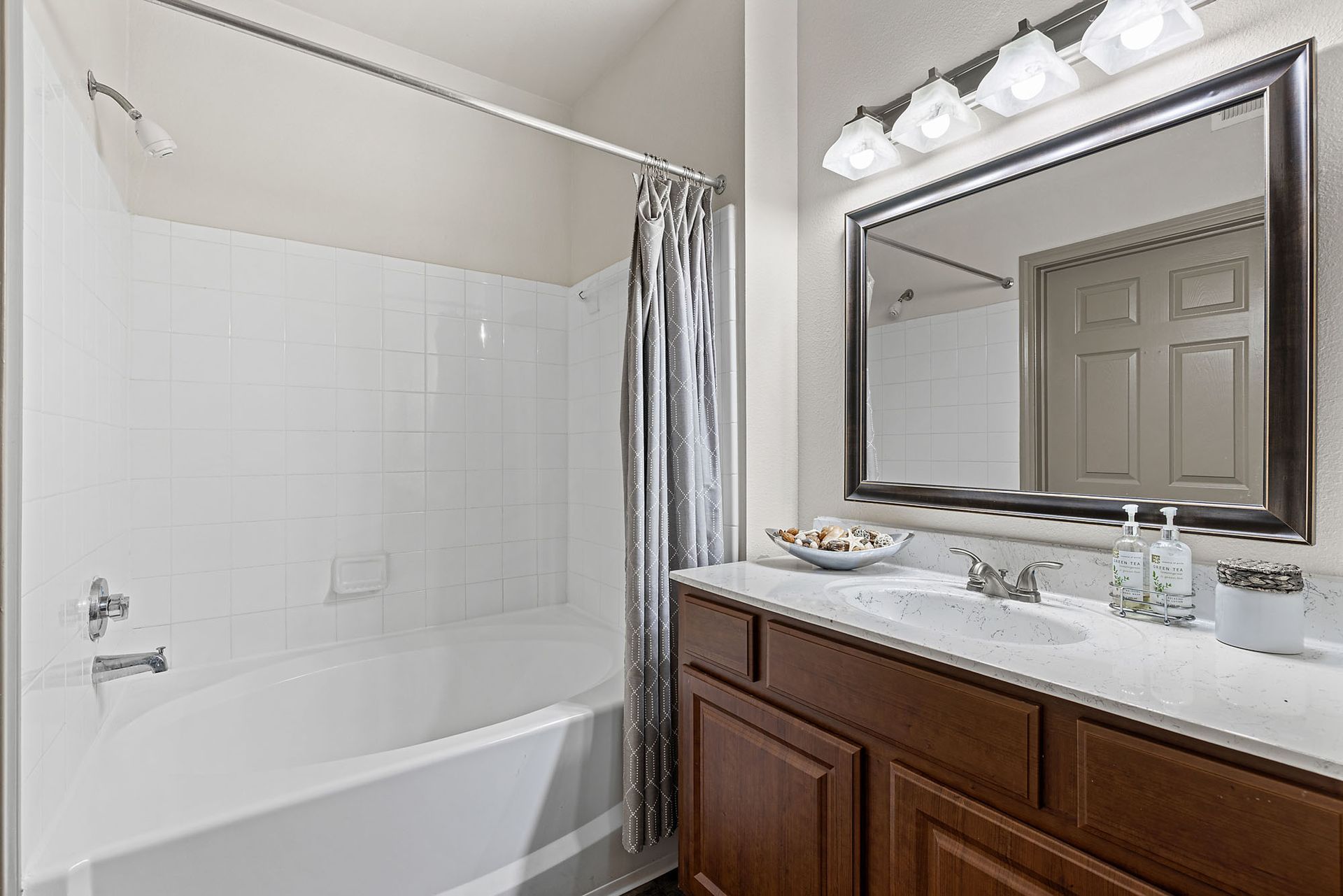 Bathroom featuring a tub/shower, white tile surround, vanity, and large framed mirror.