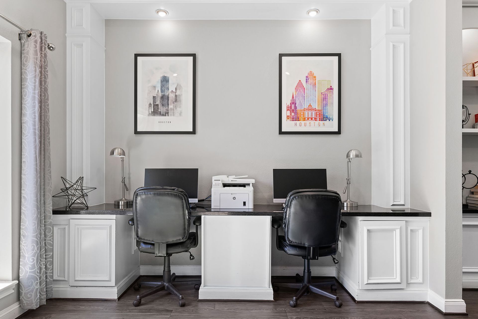 Home office nook with built-in white cabinets, dual desks and chairs, a printer, and framed city art.