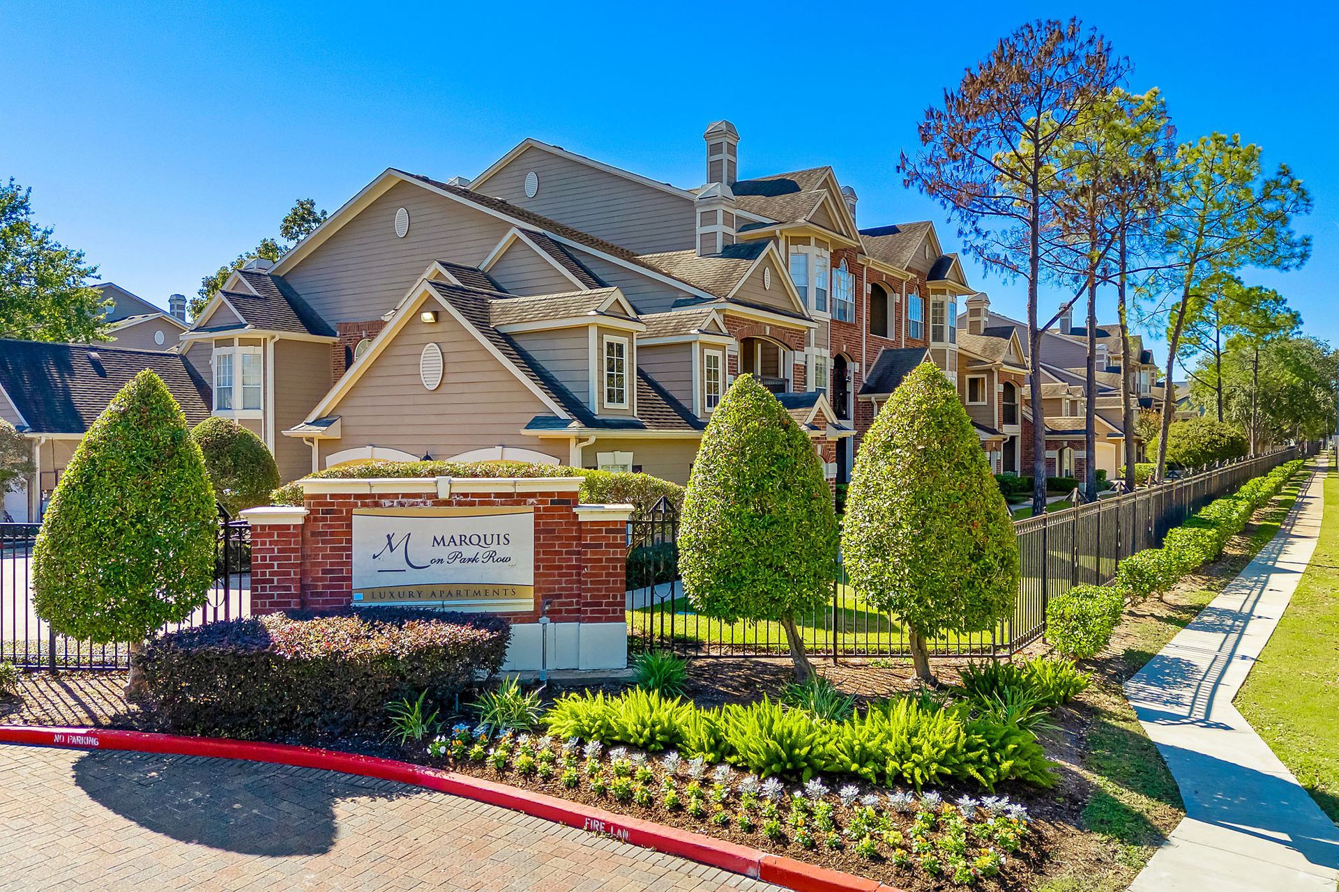 Exterior view of Marquis on Park Row luxury apartments with manicured shrubs and a gated entry.
