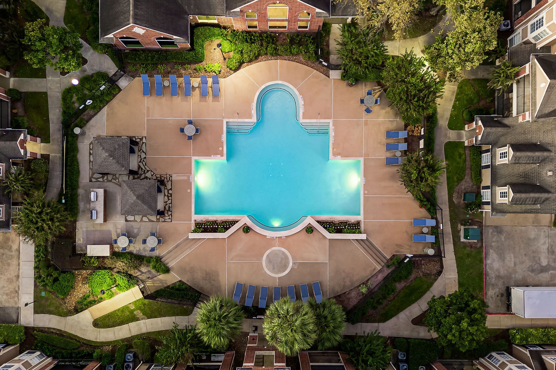 Aerial view of a large outdoor pool with lounge chairs and surrounding apartment buildings.