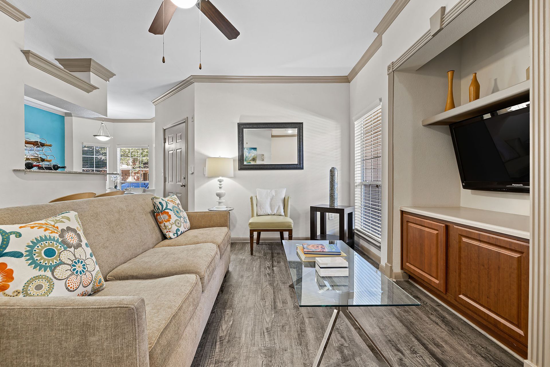 Living room with beige sofa, glass coffee table, TV cabinet, and window blinds.