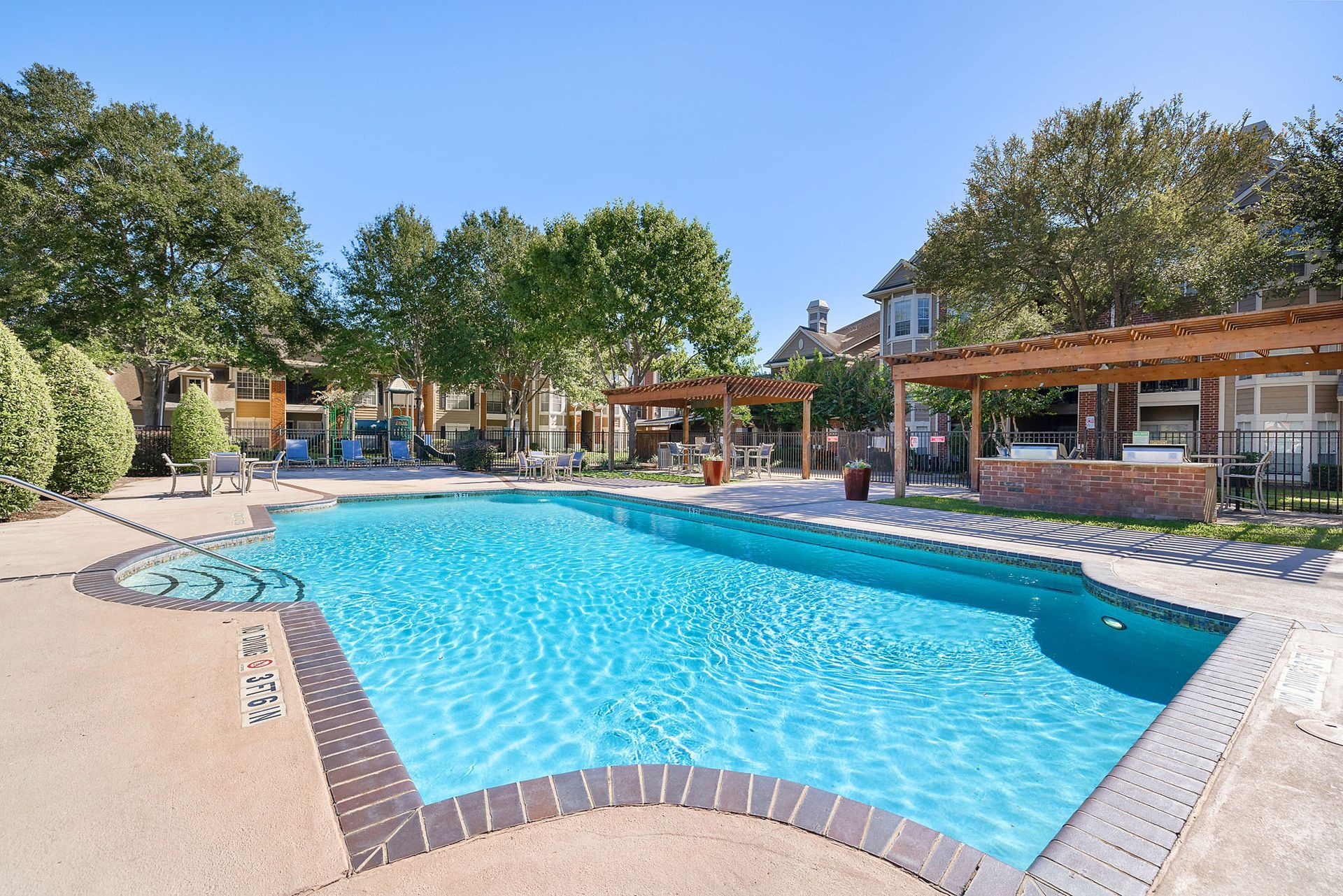 Outdoor apartment community pool with lounge chairs and pergolas.