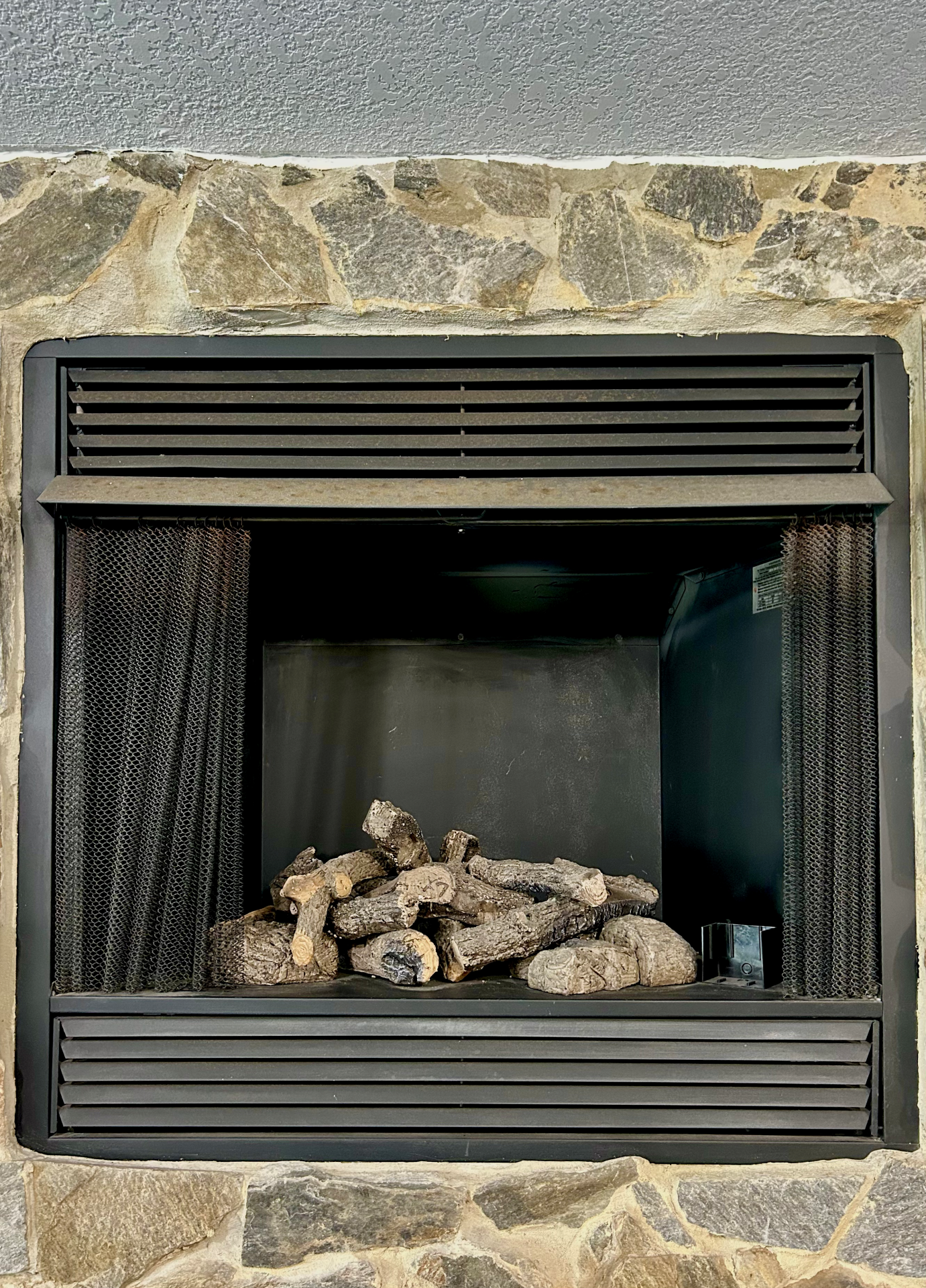 A fireplace with logs in it is built into a stone wall. - Coker Fuel