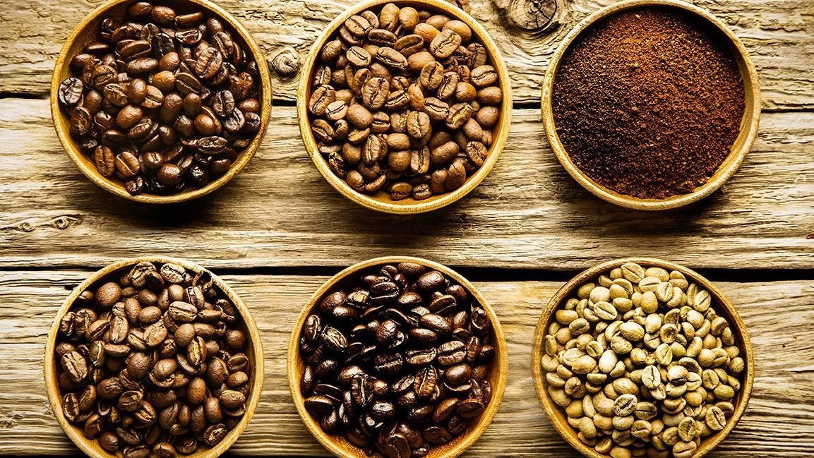 There are many different types of coffee beans in bowls on a wooden table.