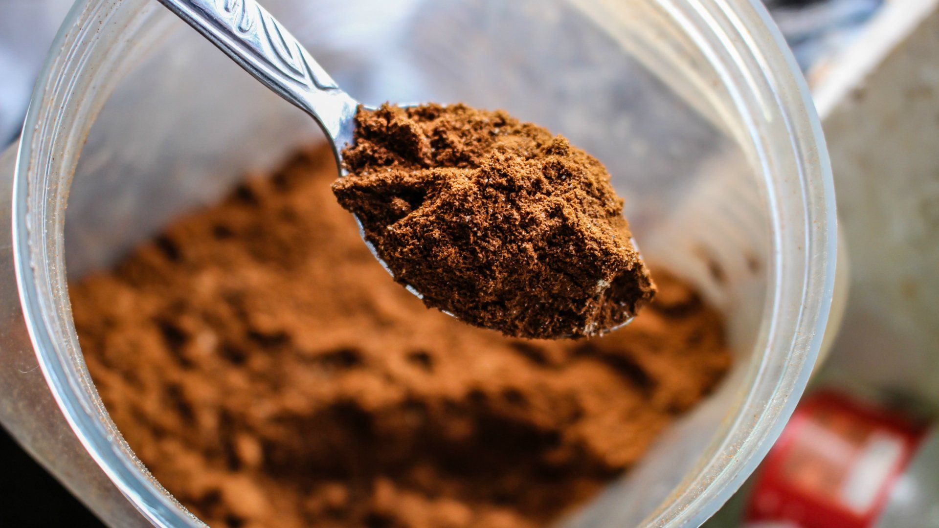 A spoon is scooping cocoa powder out of a plastic container.