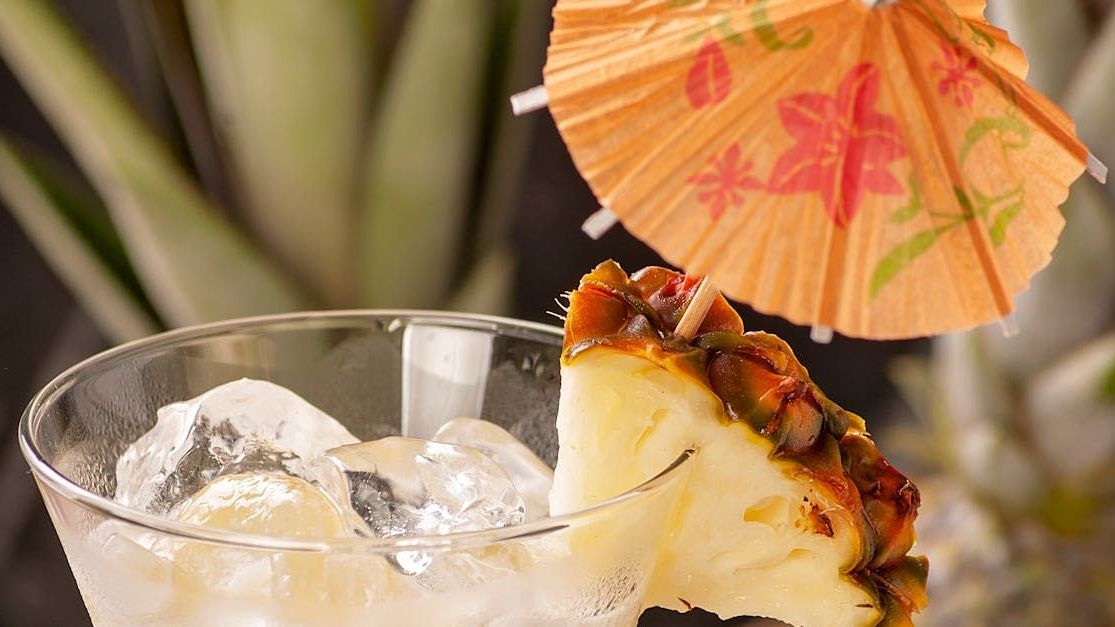 A pineapple slice is sitting on top of a martini glass with ice.