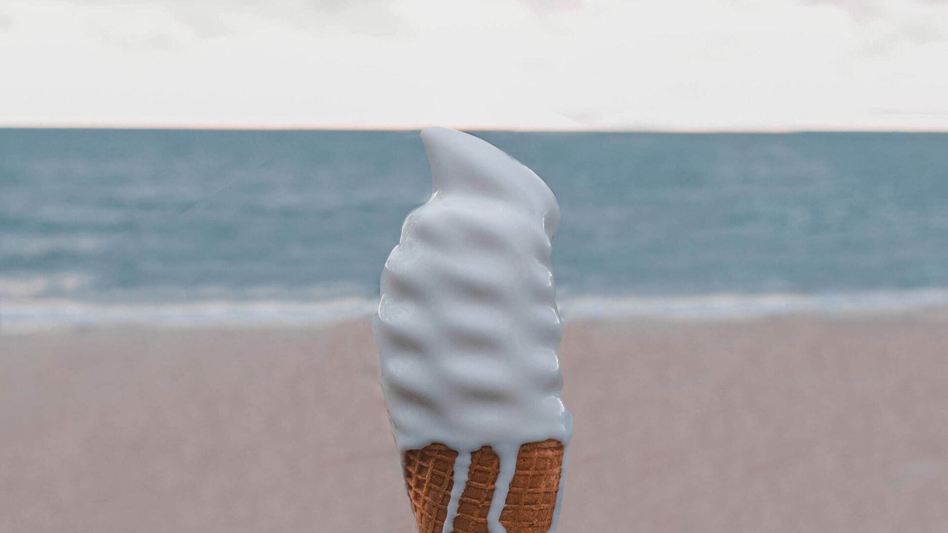 A close up of an ice cream cone on a beach with the ocean in the background.