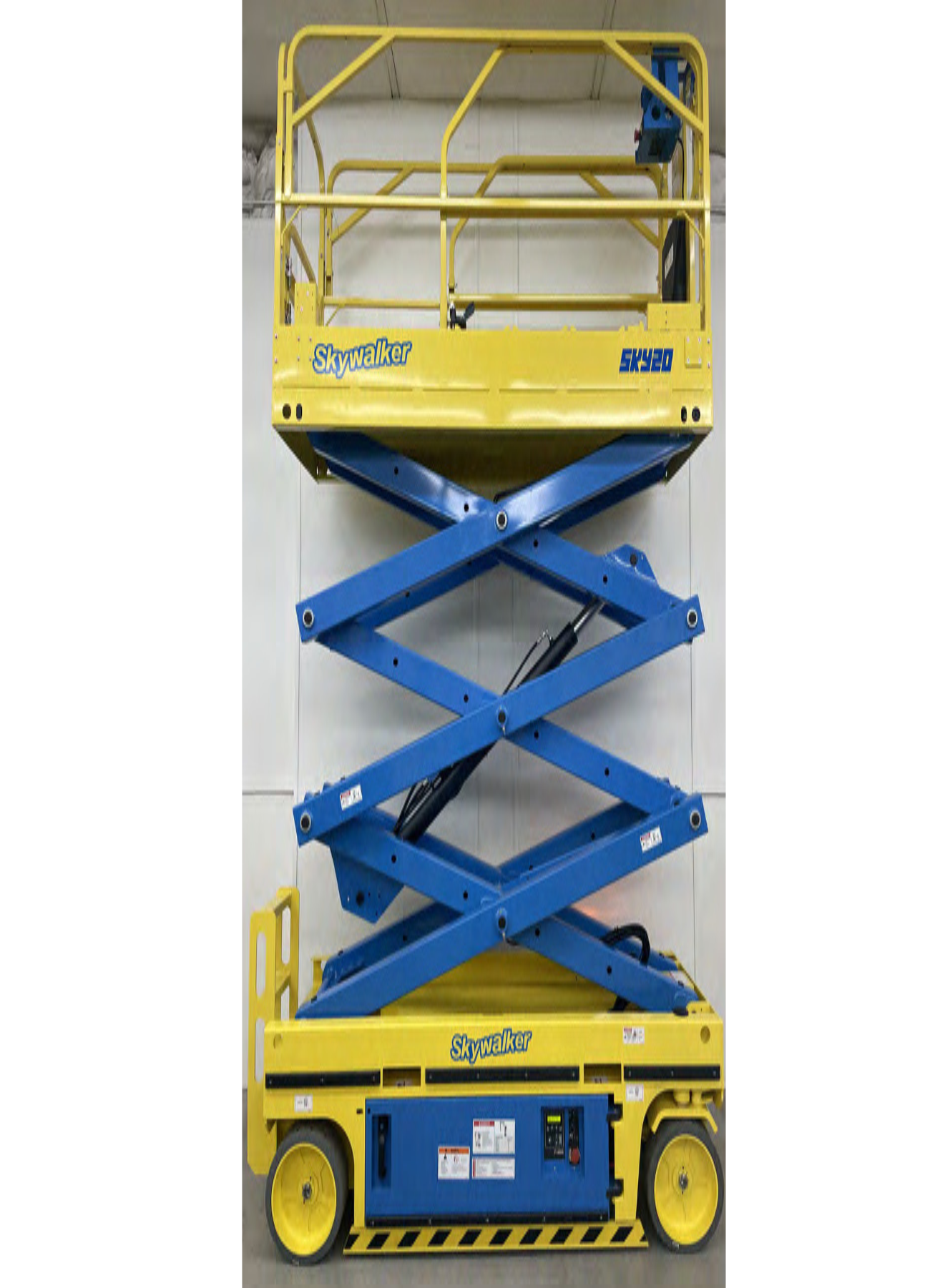 A yellow and blue scissor lift is sitting in front of a wall.