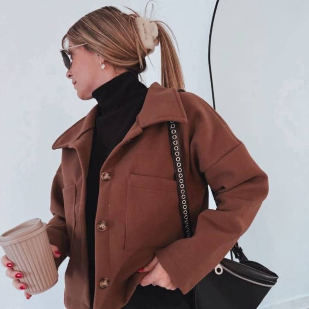 Una mujer con una chaqueta marrón sostiene una taza de café.
