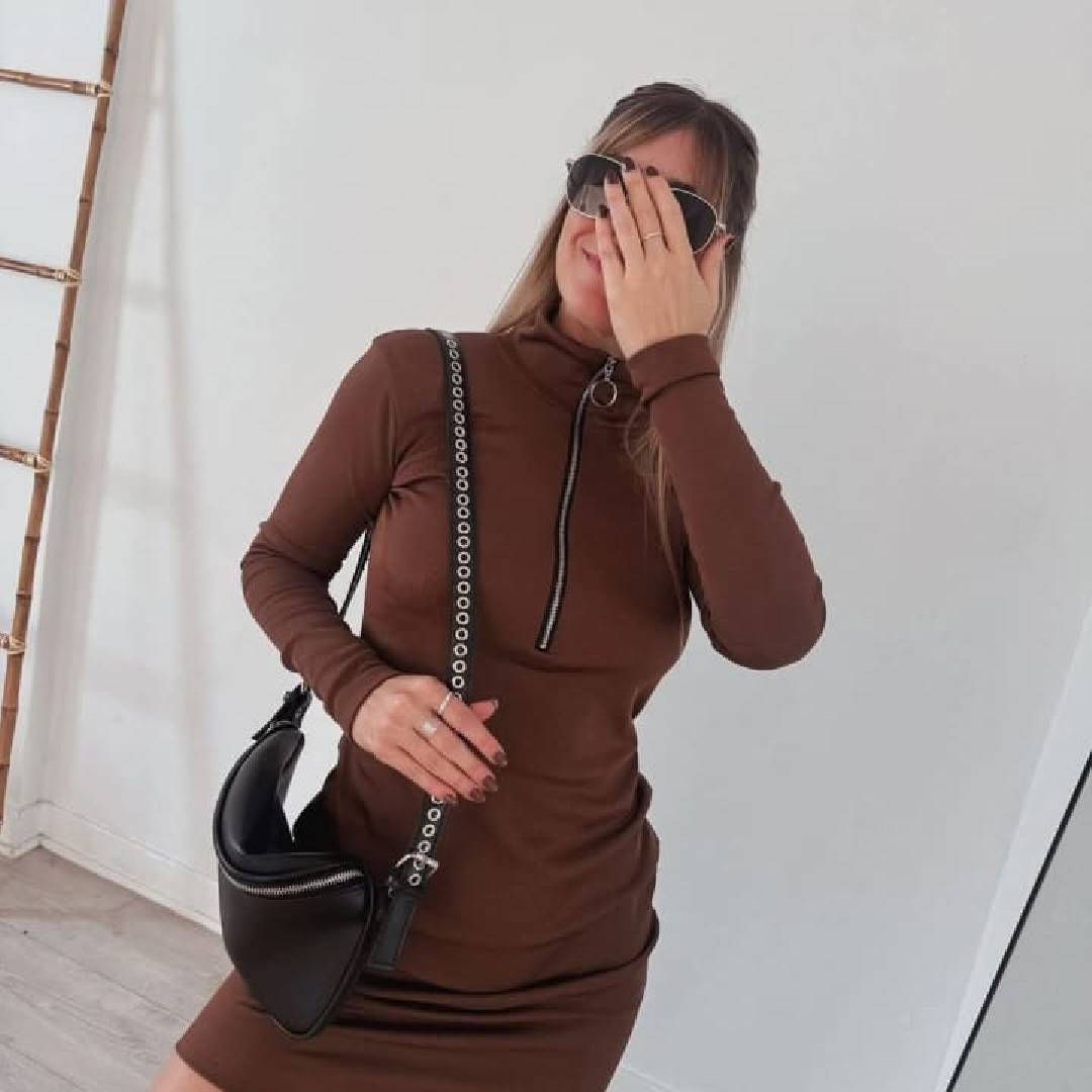 Una mujer con un vestido marrón cubriéndose la cara con la mano.