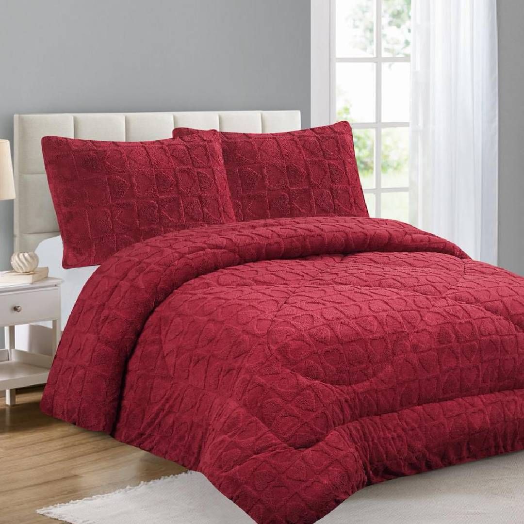 Una cama con un edredón rojo y almohadas encima.