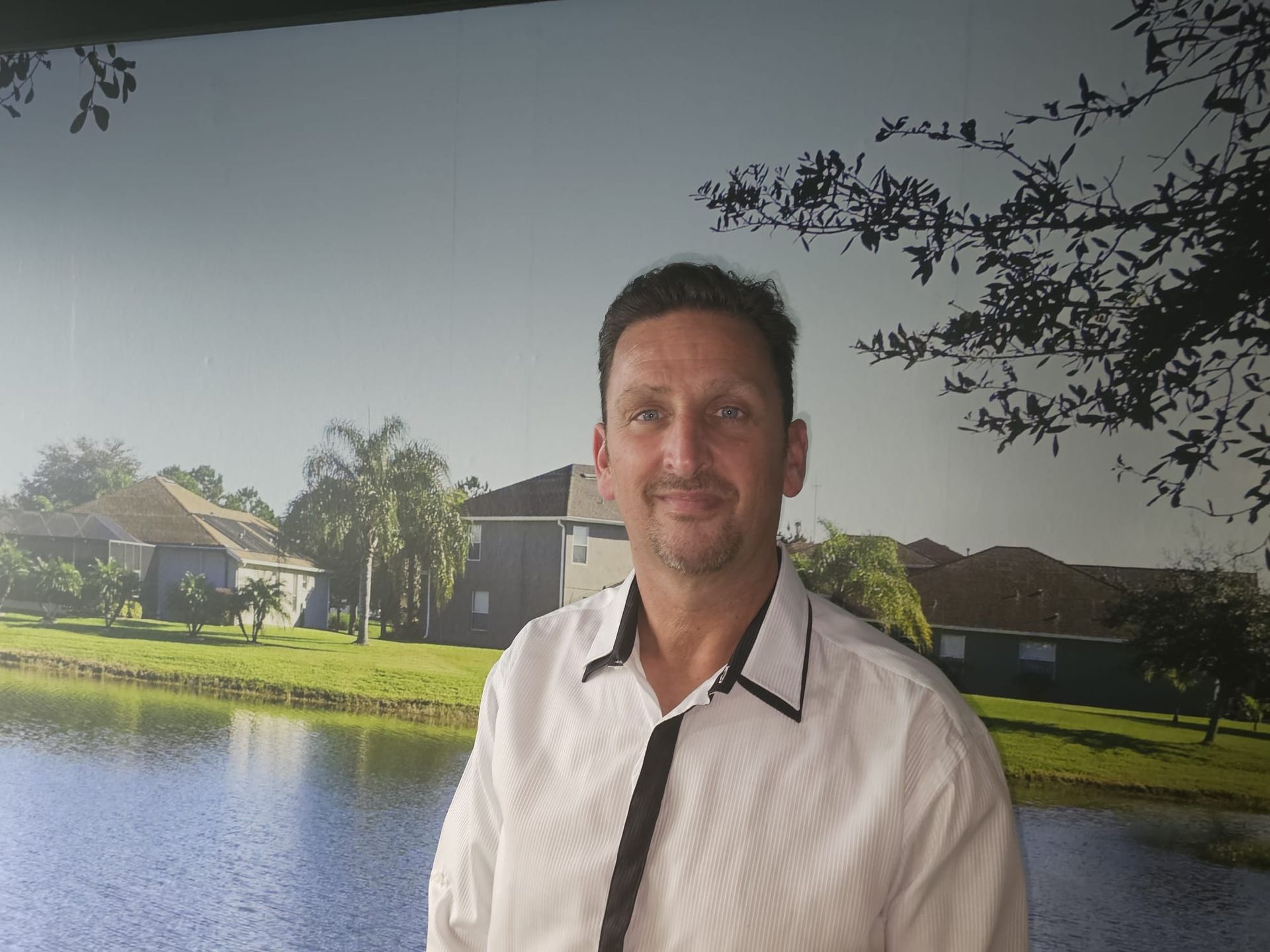 Een man in een wit overhemd en stropdas staat voor een meer