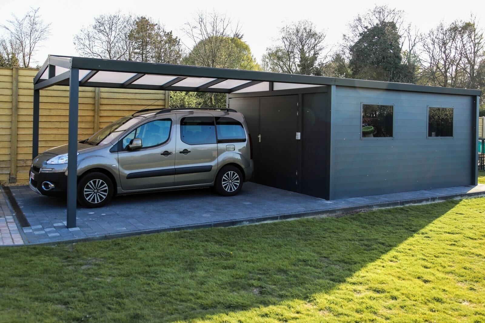 Een auto staat geparkeerd onder een luifel naast een garage.