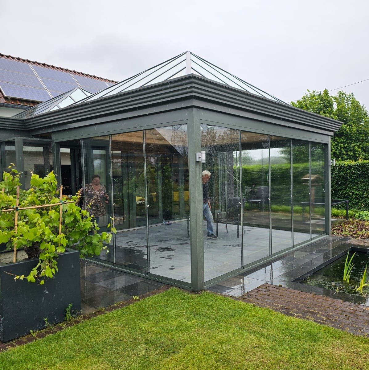Een man staat voor een glazen huis met een vijver in de achtertuin.