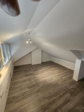 Een lege zolder met een houten vloer en een plafondventilator.