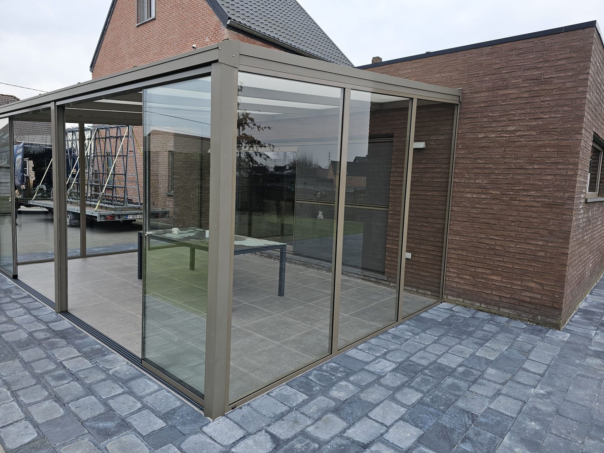 Een bakstenen huis met een glazen pergola ervoor.