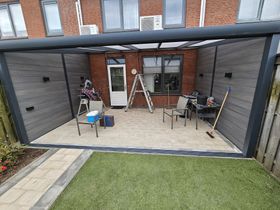 Een terras met stoelen, een tafel en een ladder voor een bakstenen gebouw.