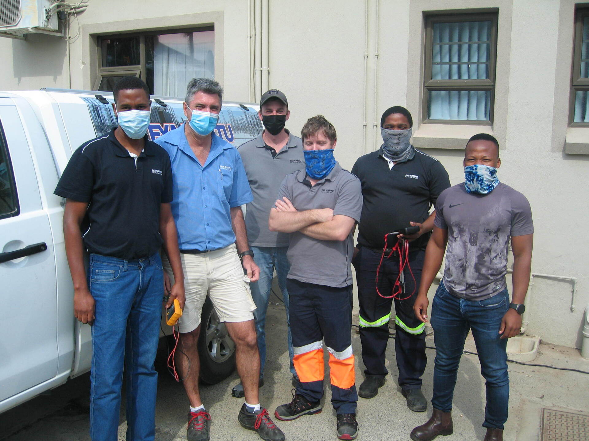 A group of men wearing face masks are standing in front of a truck.