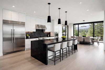 A well-lit, neutral-toned kitchen with a dark island, light countertops, wooden floor, and recessed lighting.