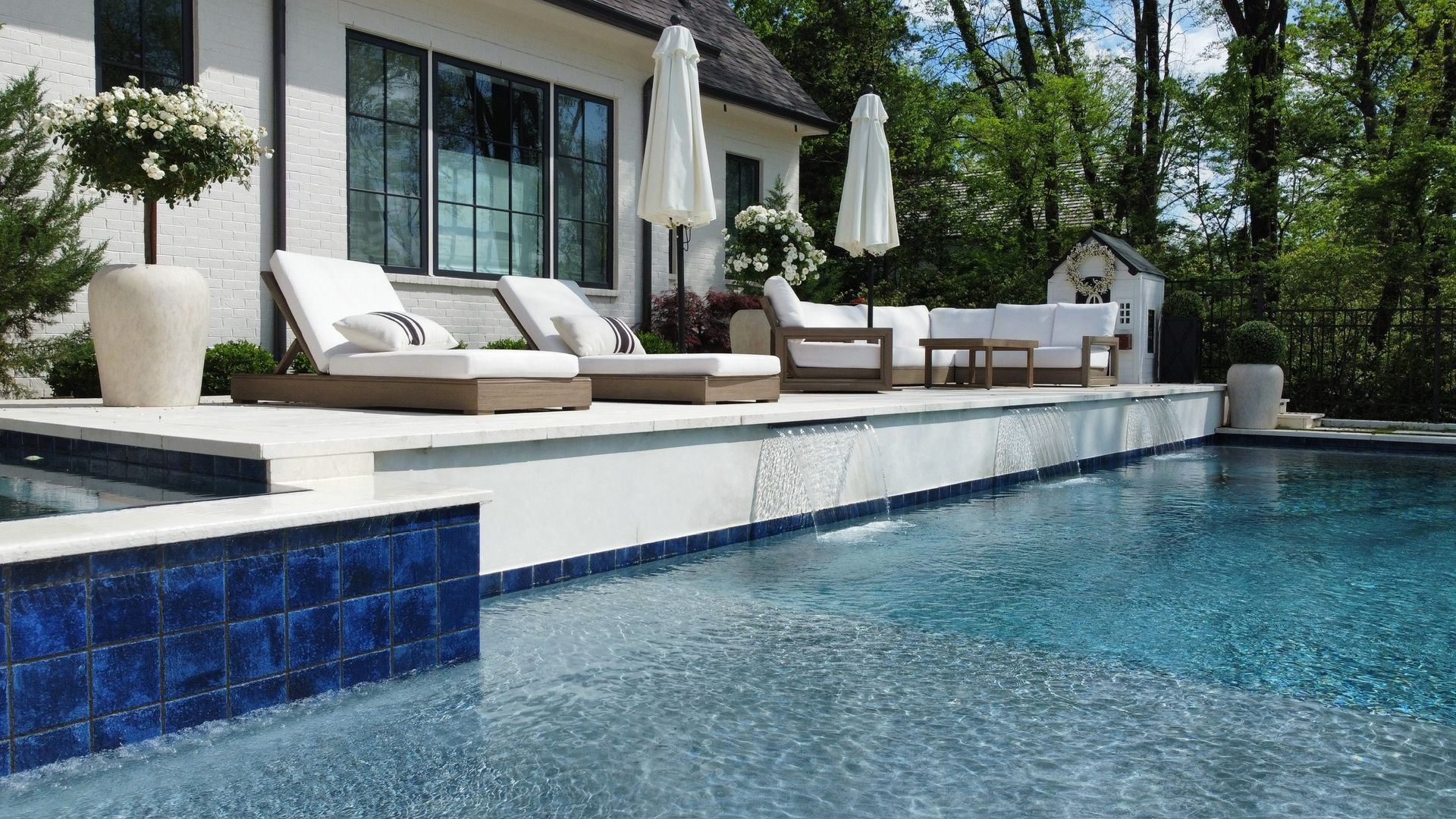 Luxury outdoor pool with lounge chairs and white patio furniture. Clear blue water and a white exterior home.
