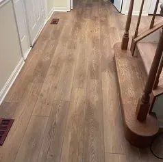 Hallway with light brown wood-look flooring. Wooden staircase on right, white door on left.