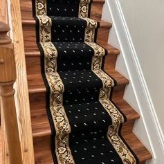Black carpet runner with patterned border on wooden stairs.