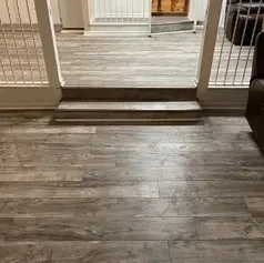 Hardwood-look flooring leads to steps and a room, with railings and a glimpse of a door.