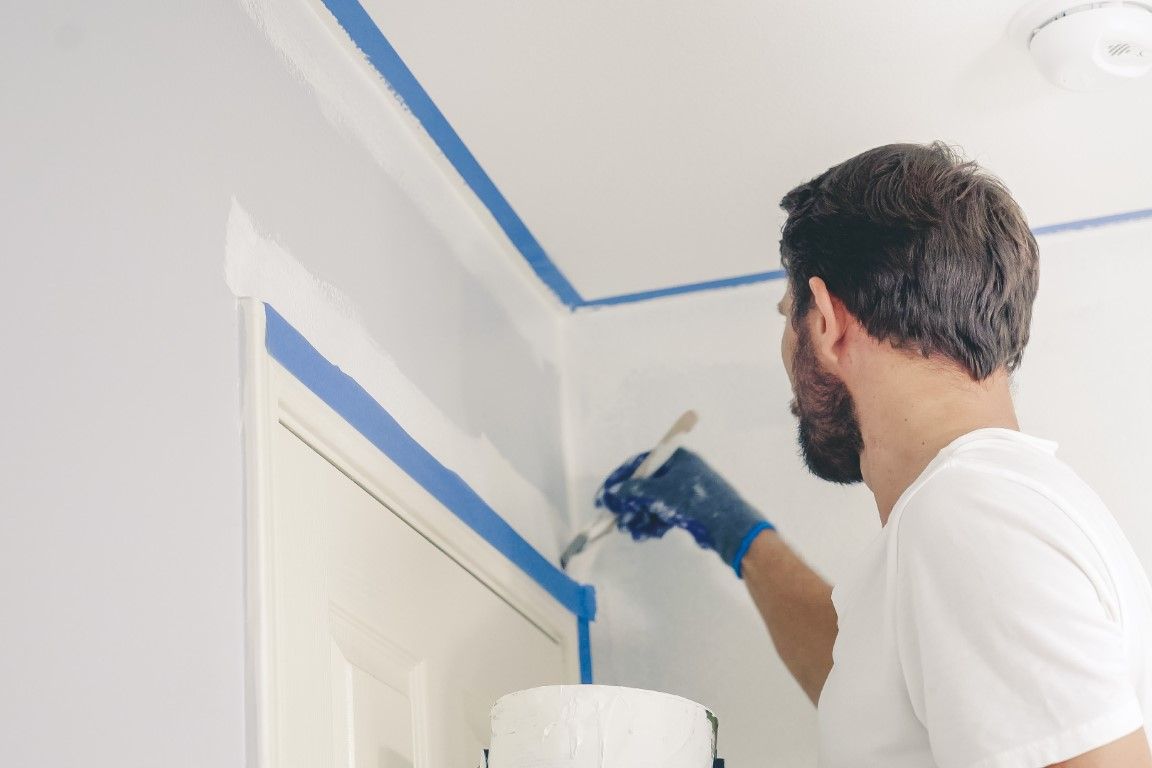 Man painting a wall with blue painter’s tape around the ceiling and doorframe