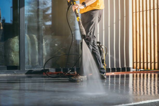 Person pressure-washing a wet floor with a spray wand near a building entrance