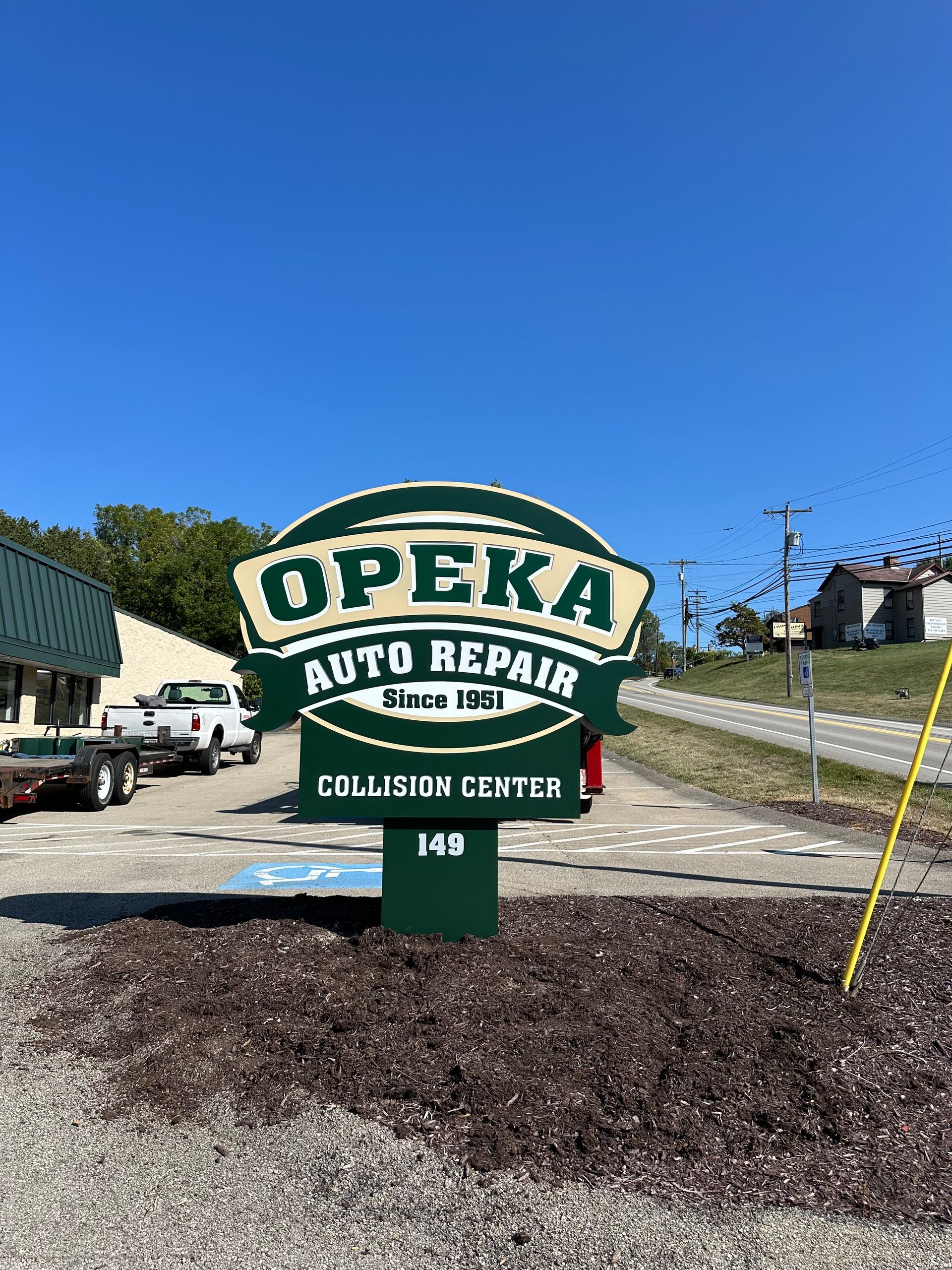 Sign for OPEKA Auto Repair, a collision center, on a sunny day.