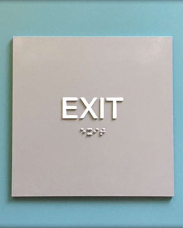 Gray exit sign with white lettering and Braille on a blue wall.