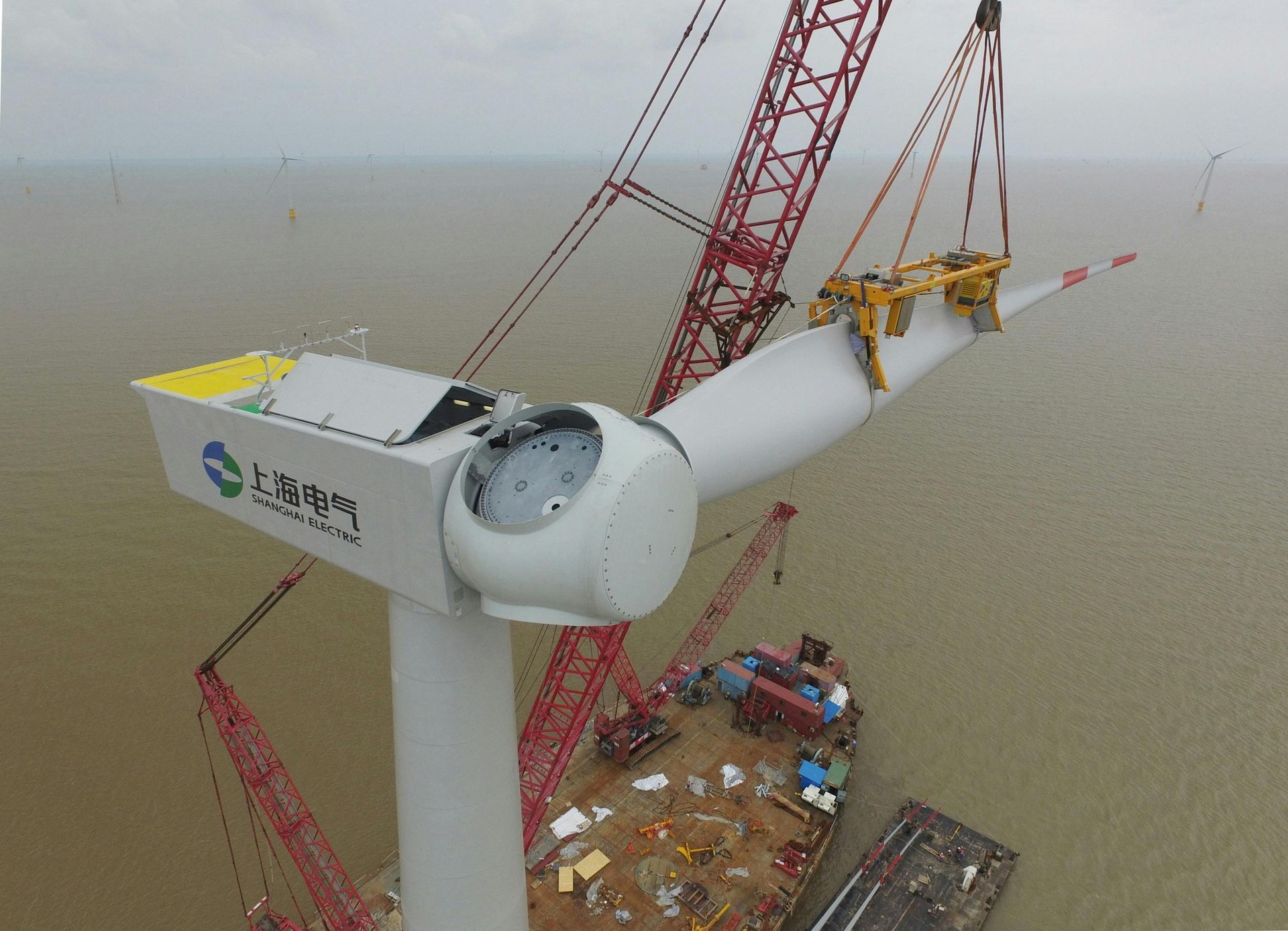 Wind turbine being assembled offshore by crane.