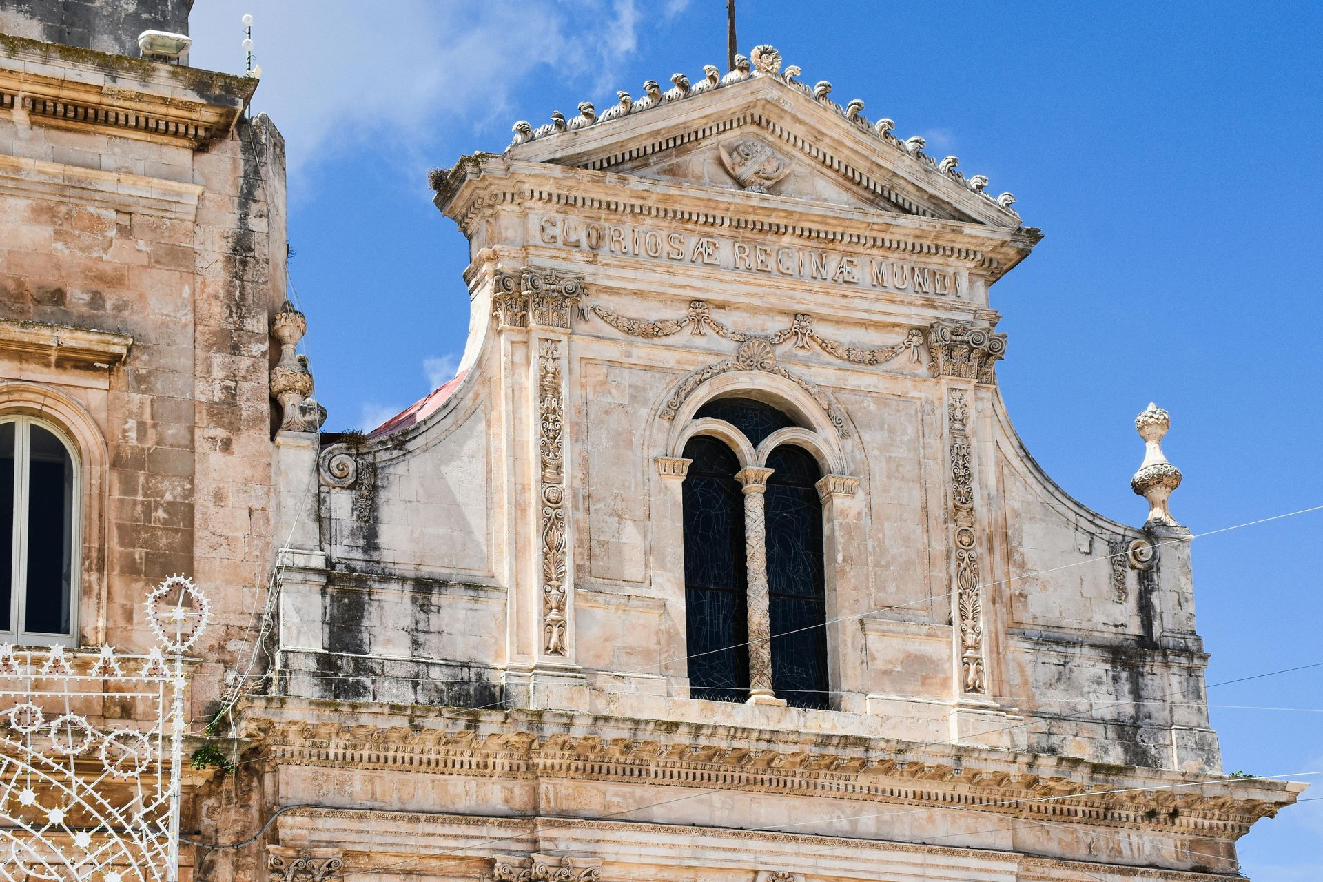 Ornate, cream-colored Baroque church facade against a blue sky, featuring a window and decorative carvings.