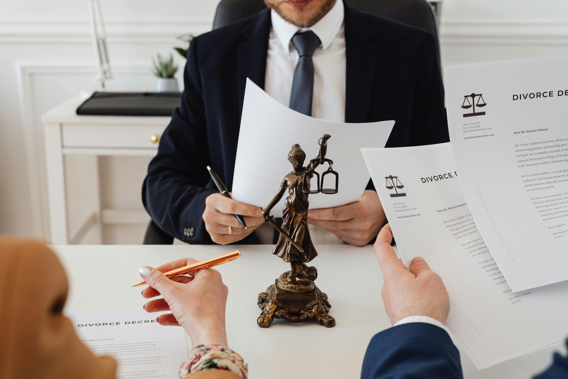 Lawyer reviewing documents with clients at a desk; scales of justice statue.