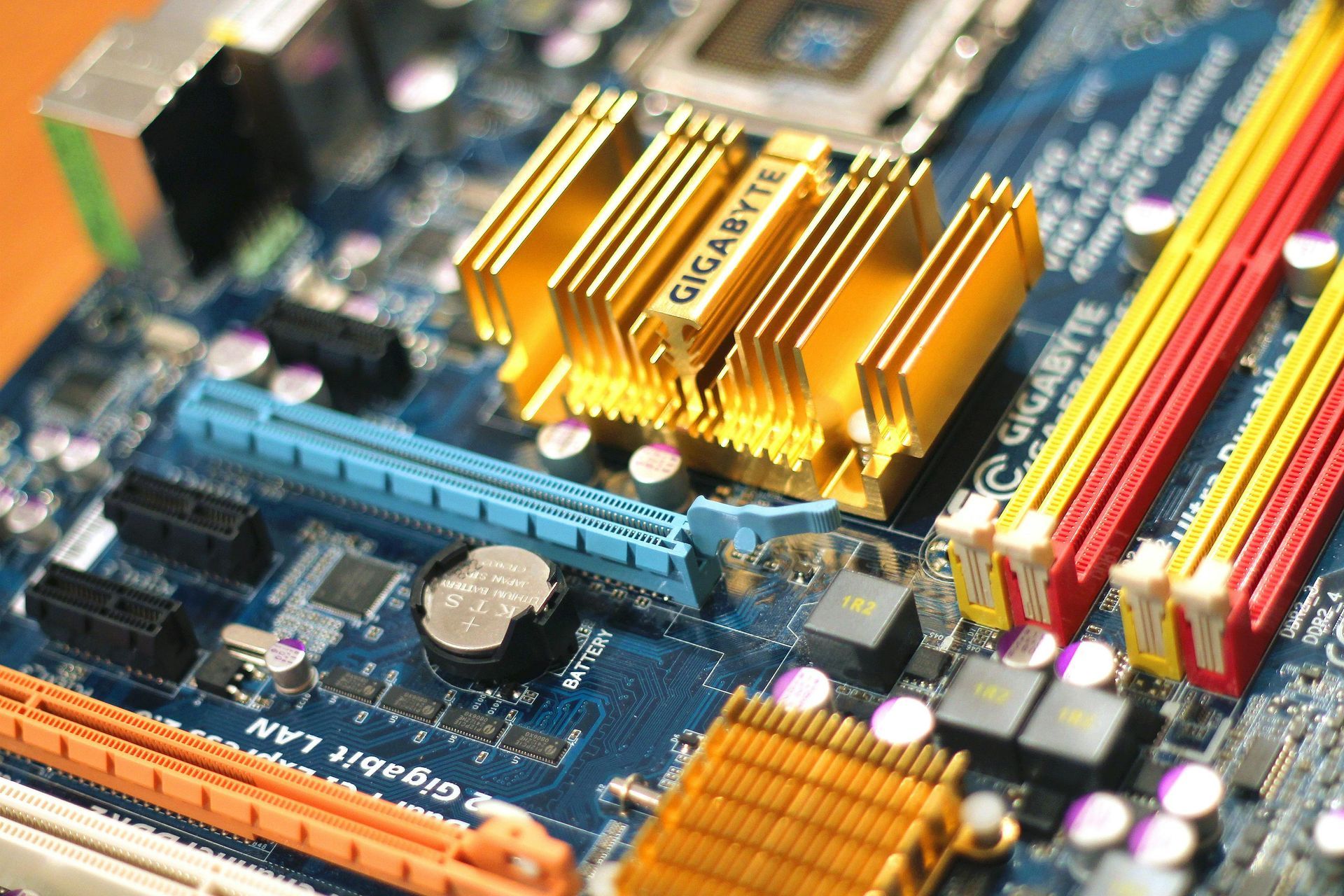 Close-up of a blue circuit board with gold heat sinks, and RAM slots in blue, red, and yellow.