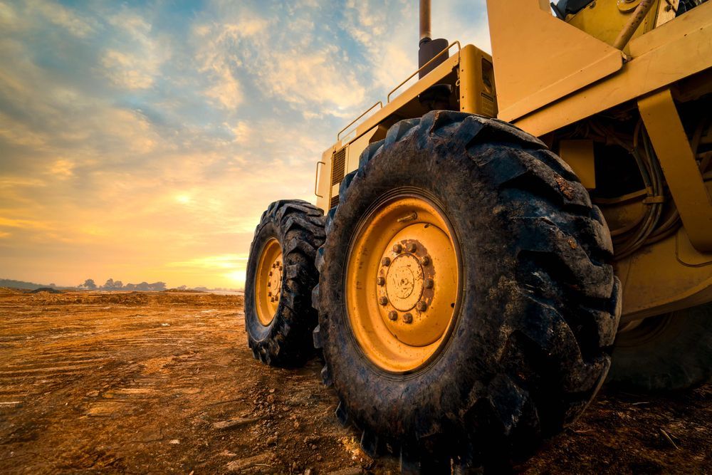 A bulldozer is parked in a dirt field at sunset.