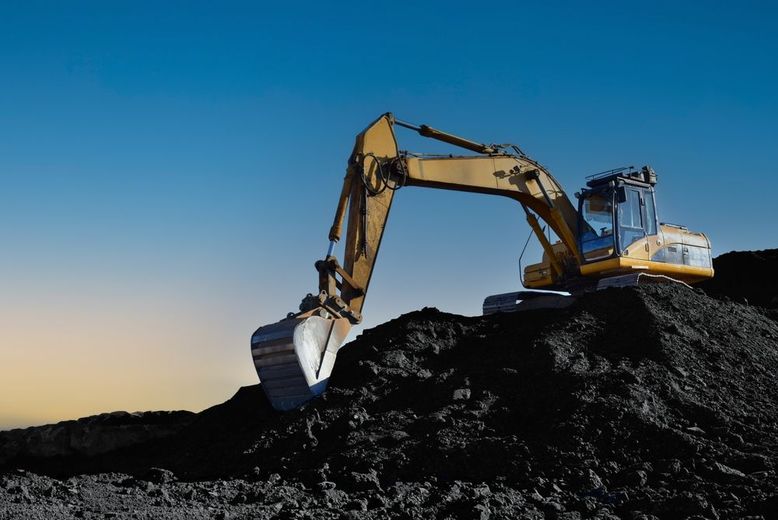 A yellow excavator is sitting on top of a pile of dirt.