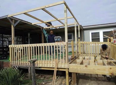 Construction of a wooden deck and pergola on a house. Men work on framing and decking.