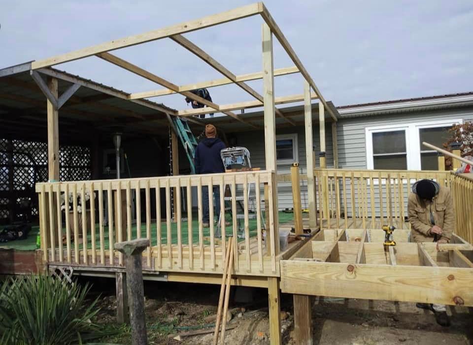 Construction of a wooden deck and pergola outside a house; workers install framing.