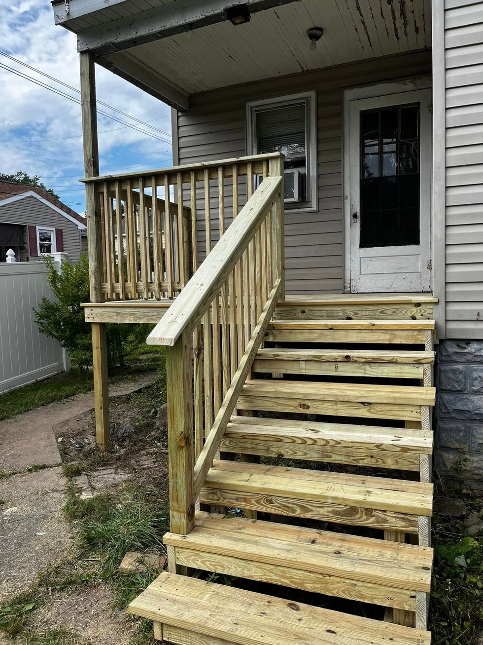 Wooden steps leading up to a porch with a railing and door. The siding is beige. Cloudy day.