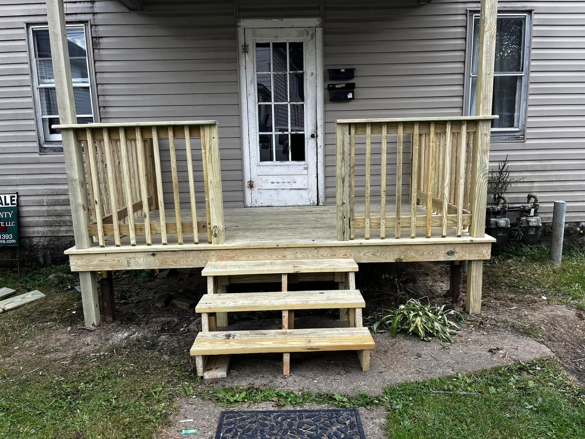 Exterior of a house with a wooden porch and steps leading to a white door.
