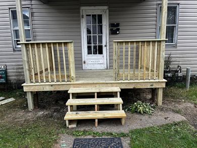 A weathered porch with wooden railing and steps leading to a white door.