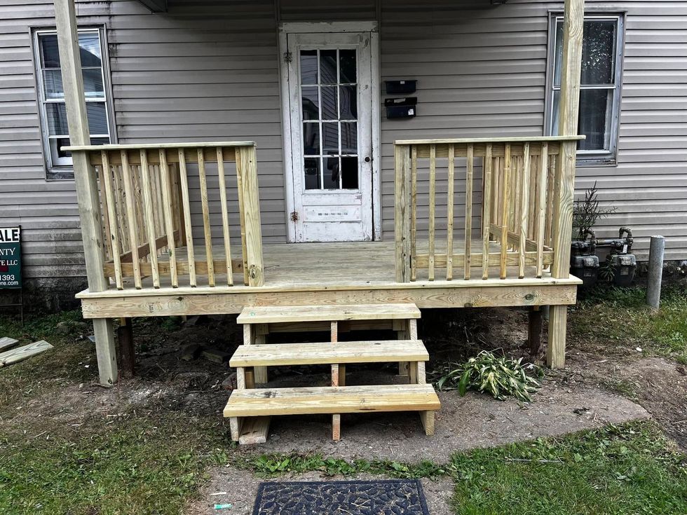 Exterior of a house with a wooden porch and steps leading to a white door.